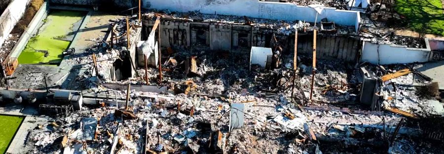 Aerial view of a residential structure fire site with exposed concrete foundation walls and debris.
