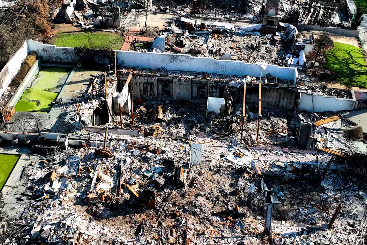 Aerial view of a residential structure fire site with exposed concrete foundation walls and debris.